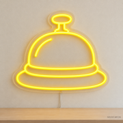 Watermarked concept mockup of Mini Desk Bell LED Neon Sign in Yellow on a clear acrylic backboard.