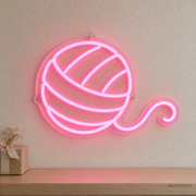 Watermarked concept mockup of the Mini Yarn Ball LED Neon Sign in Pink on a clear acrylic backboard.